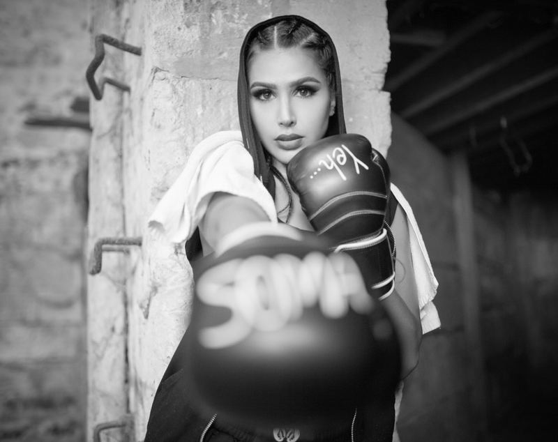 Somayeh in black and white, hood up and a towel over her shoulders, her gloved fist stretched toward the camera